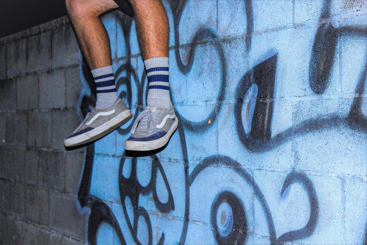 Man's legs with grey and navy socks in front of a wall with blue graffiti.