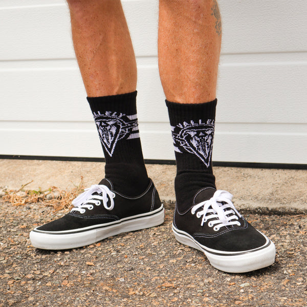 Dirty Donny x Mike Vallely Collaboration Crew Socks. Black Crew Socks with 3 white stripes on the leg. Mike Vallely's Elephant V Logo with lightning bolts in an inverted triangle on the front of the leg. "VALELLY" in all caps above the Mike V Elephant Logo.