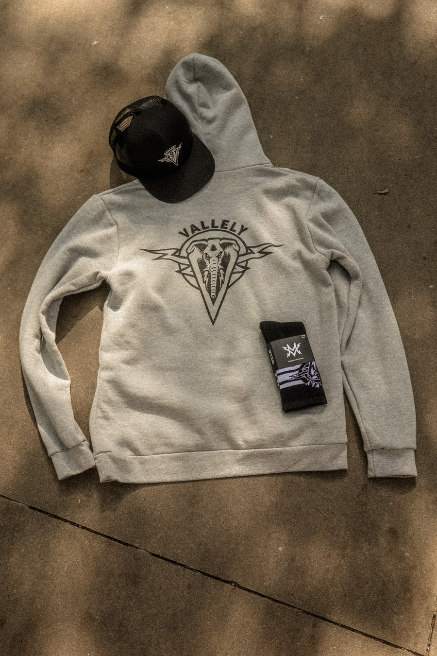 Dirty Donny x Mike Vallely Collaboration Line products: Black Logo Hat, Heather Grey Hoodie, and Black Crew Socks with custom DD x MV sock wrap.