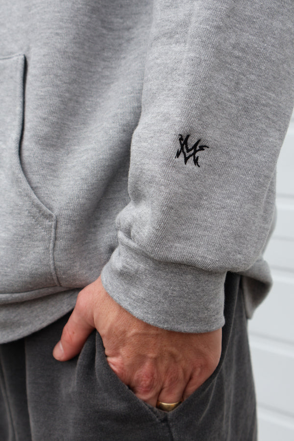 heather gray Dirty Donny x Mike Vallely Collaboration Logo Hoodie with White Pull Strings and Black logo on the front left chest area. Large Black Logo on the Back of the Hoodie. Close up shot of "MV" Initials lightning logo on the lower left arm of the hoodie.