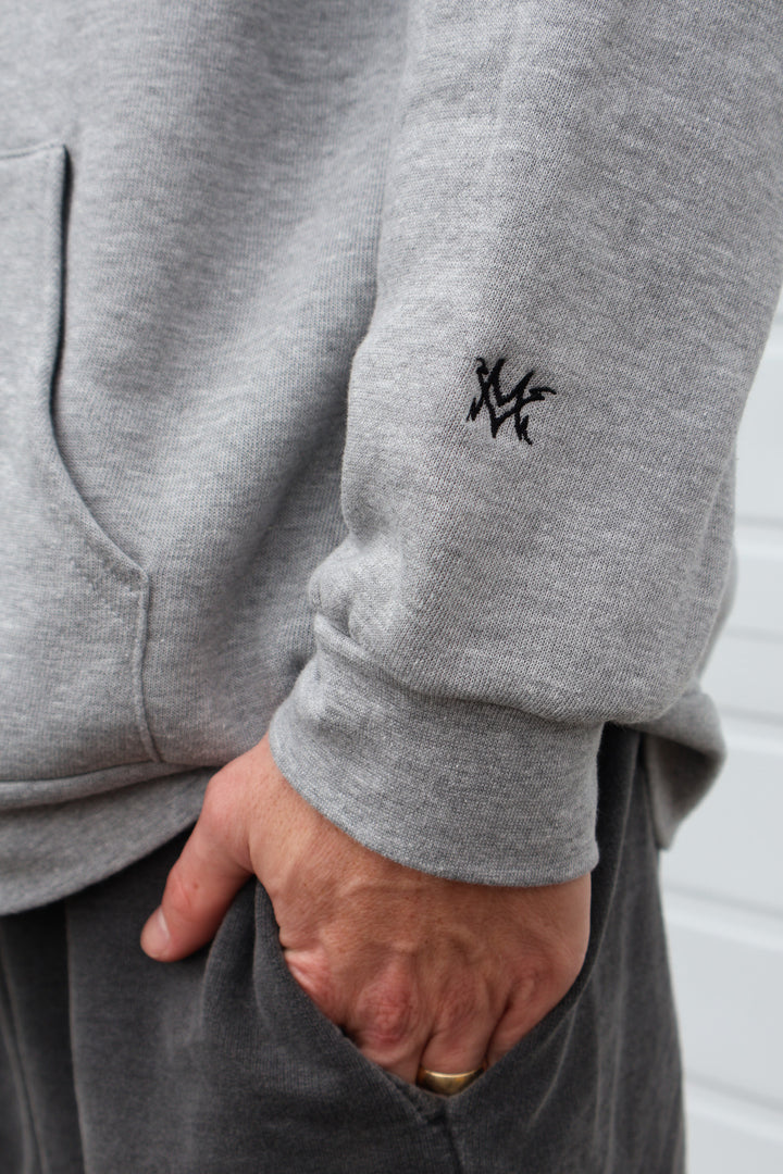 heather gray Dirty Donny x Mike Vallely Collaboration Logo Hoodie with White Pull Strings and Black logo on the front left chest area. Large Black Logo on the Back of the Hoodie. Close up shot of "MV" Initials lightning logo on the lower left arm of the hoodie.