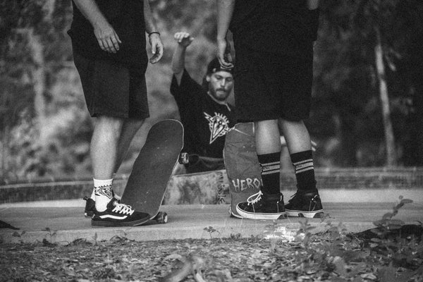 Scene of two skaters standing at the edge of a bowl. They are hanging out and talking, one foot on their skateboards, each in either a white or black Dirty Donny x Mike V Collaboration Sock colorways.