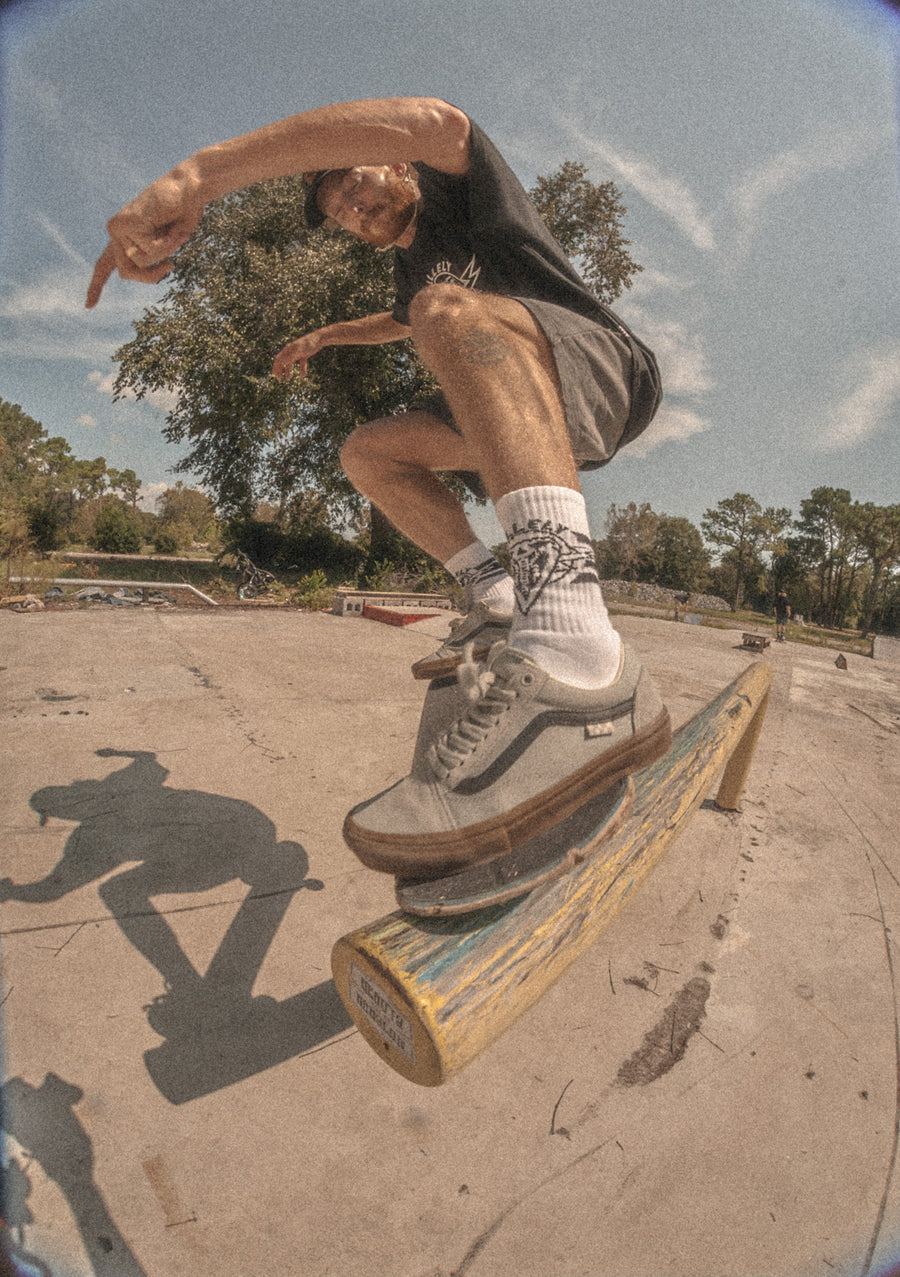 Skateboarder riding a rail and wearing Dirty Donny x Mike Vallely Black Hat with Logo, Black Tee with Logo, and White Crew socks.